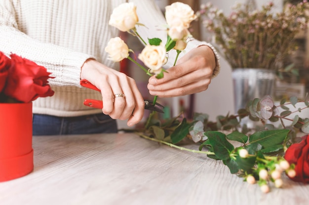 Il venditore di negozi di fiori prepara le rose per creare un bouquet potandole con potatori
