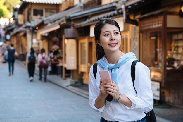 il viaggiatore con zaino e sacco a pelo femminile asiatico allegro sta sorridendo e guardando in lontananza con un telefono cellulare in mano mentre si gode la visita della via di sannen zaka a Kyoto in Giappone