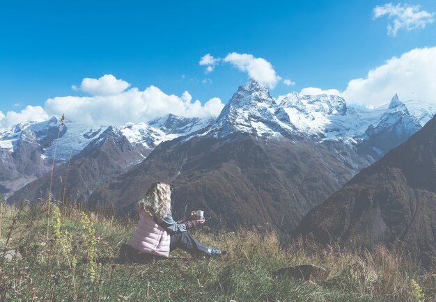 Il viaggiatore della donna beve il caffè con una vista del paesaggio della montagna. Una giovane turista beve una bevanda calda da una tazza e si gode il paesaggio in montagna. Concetto di trekking.