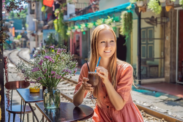 Il viaggiatore della giovane donna beve il caffè seduto dai binari ferroviari che attraversano la zona residenziale dentro