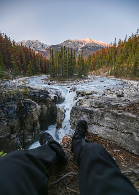 Il viaggiatore delle gambe si siede allungando sulle cascate di Sunwapta in Icefields Parway al parco nazionale di Jasper, Canada