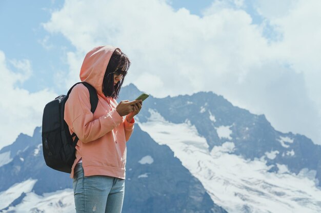 Il viaggiatore femminile sta con lo smartphone in montagna Turista che naviga sul cellulare contro il cielo nuvoloso in una giornata di sole in un terreno montuoso