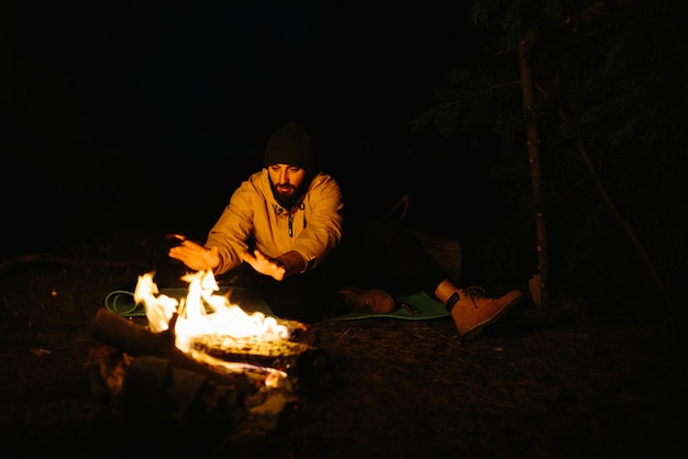 Il viaggiatore riposa vicino al fuoco notturno Fornito riparo dai rami per dormire con una lampada a cherosene e un fuoco circondato da pietre