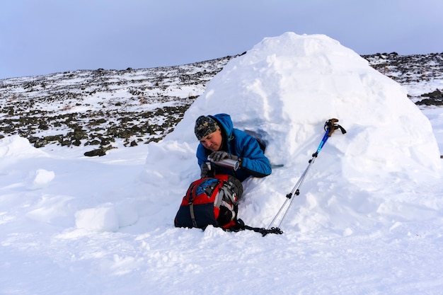 Il viaggiatore si versa una bevanda calda da un thermos seduto in un igloo di una casa innevata