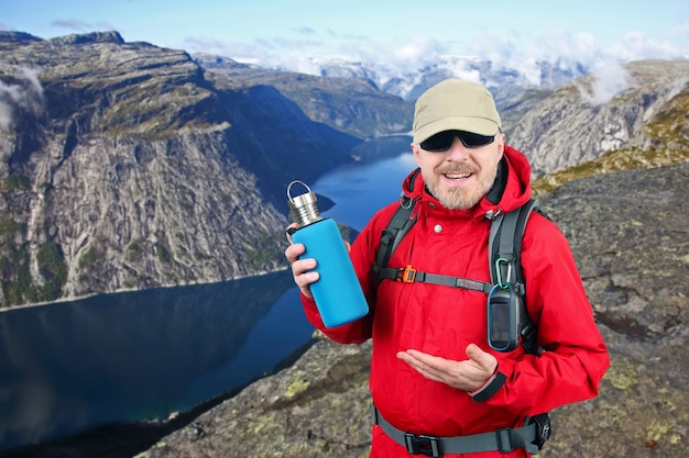 Il viaggiatore turistico in una giacca rossa mostra una bottiglia di metallo per l'acqua