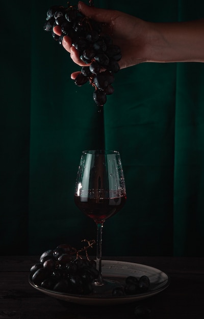 Il vino rosso gocciola da una vite in un bicchiere. Sfondo scuro, foto verticale.