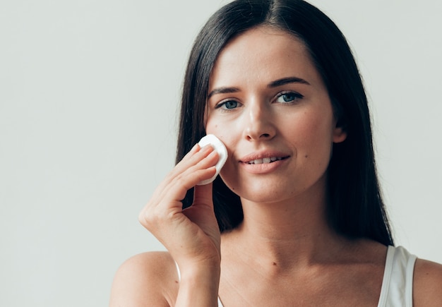 Il viso della donna del batuffolo di cotone rimuove il trucco naturale della pelle sana. Colpo dello studio.