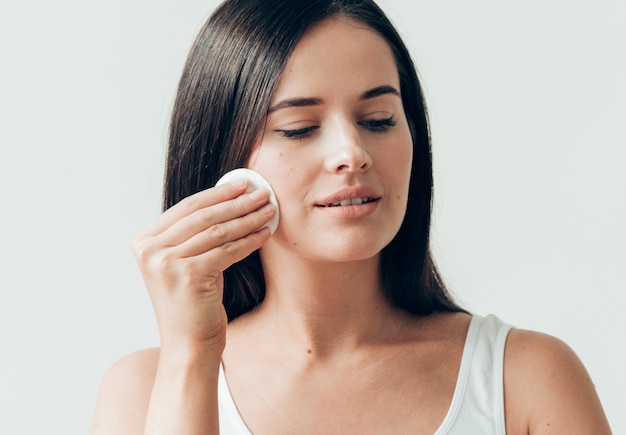 Il viso della donna del batuffolo di cotone rimuove il trucco naturale della pelle sana. Colpo dello studio.