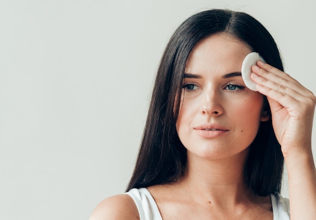 Il viso della donna del batuffolo di cotone rimuove il trucco naturale della pelle sana. Colpo dello studio.