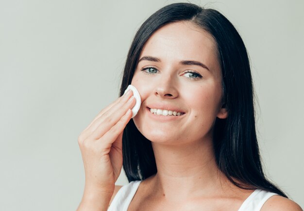 Il viso della donna del batuffolo di cotone rimuove il trucco naturale della pelle sana. Colpo dello studio.