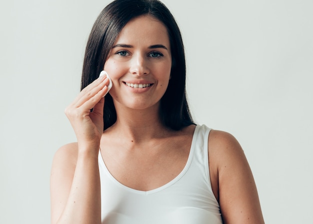 Il viso della donna del batuffolo di cotone rimuove il trucco naturale della pelle sana. Colpo dello studio.