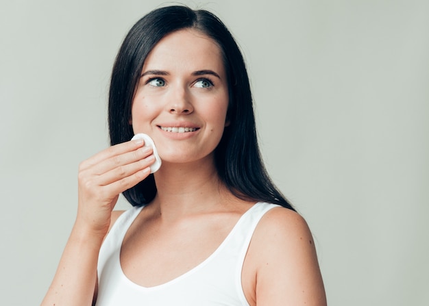 Il viso della donna del batuffolo di cotone rimuove il trucco naturale della pelle sana. Colpo dello studio.