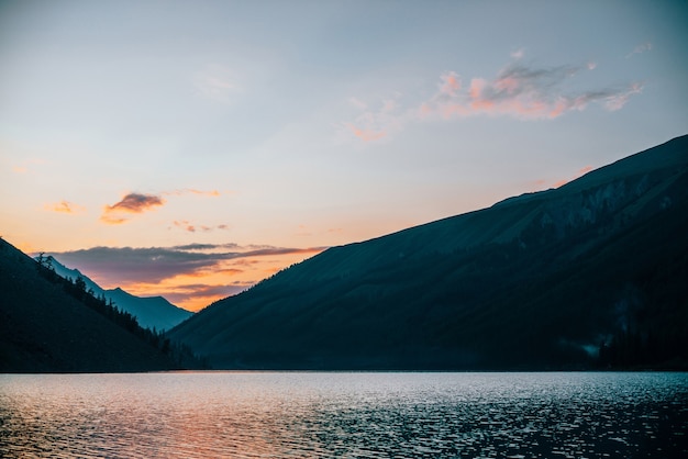 Il vivido cielo all'alba si riflette nel puro lago alpino vicino alle sagome di montagna all'alba.