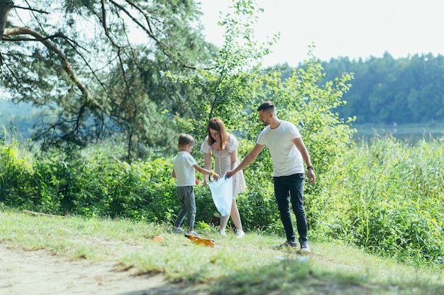 Il volontario della famiglia pulisce i rifiuti in natura. Padre e madre, genitori, figli, figli volontari di famiglia in una giornata di sole che puliscono le bottiglie dei rifiuti nella foresta di detriti piegati in un sacchetto di plastica