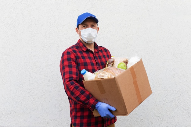 Il volontario in una maschera protettiva con una scatola di cibo, donazione