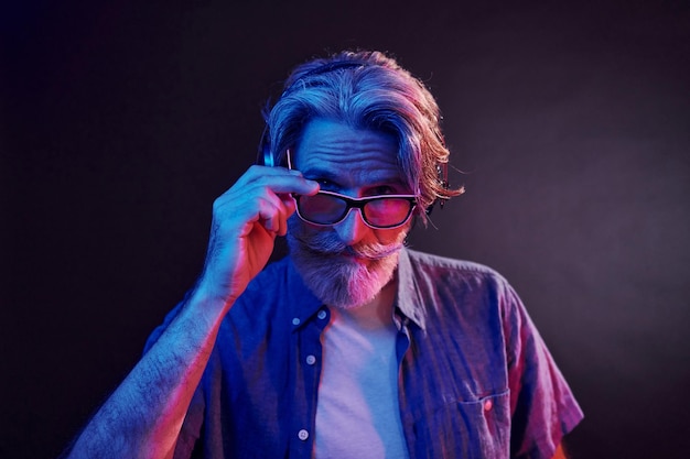 Illuminazione al neon in cuffia L'uomo anziano moderno ed elegante con capelli grigi e barba è al chiuso