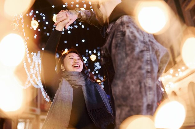 Illuminazione artificiale di ghirlande Felice coppia multirazziale insieme all'aperto in città per celebrare il nuovo anno