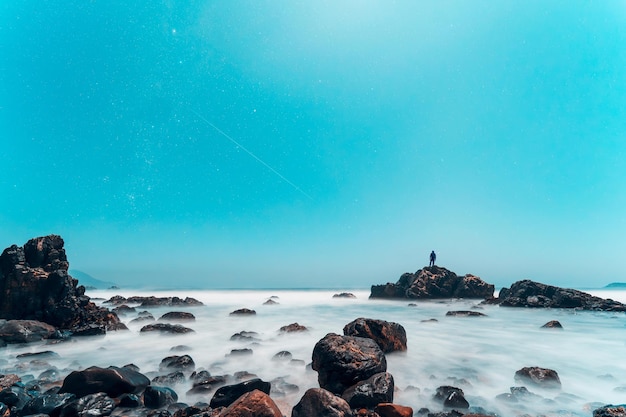 Illuminazione della luna sul mare e rocce sulla costa di notte con una silhouette sullo sfondo