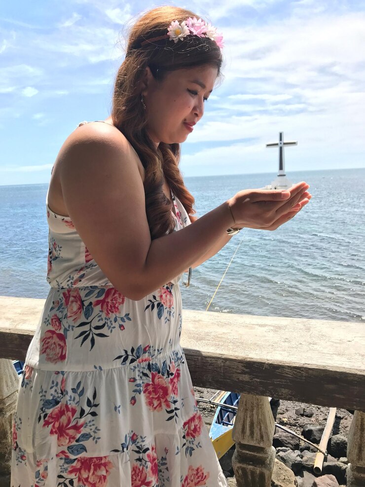 Foto illusione ottica di una giovane donna che porta una croce di cimitero affondato contro il mare