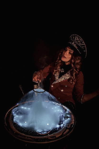 Illusionista del mago della donna del circo che mostra le bolle di sapone mostrano sul ripiano del tavolo a sfondo nero