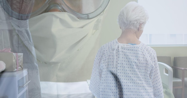 Illustrazione digitale di una persona che indossa una maschera facciale e occhiali protettivi su una paziente anziana in piedi in una stanza d'ospedale sullo sfondo. Medicina sanità pubblica pandemia coronavirus Covi