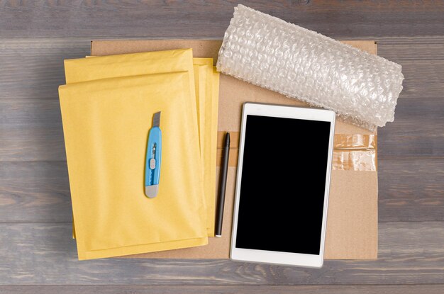 Imballaggio a bolle per smartphone con scatola di cartone e strumenti di imballaggio Il concetto di imballaggio di pacchi per un negozio online Vista dall'alto Sfondo in legno marrone