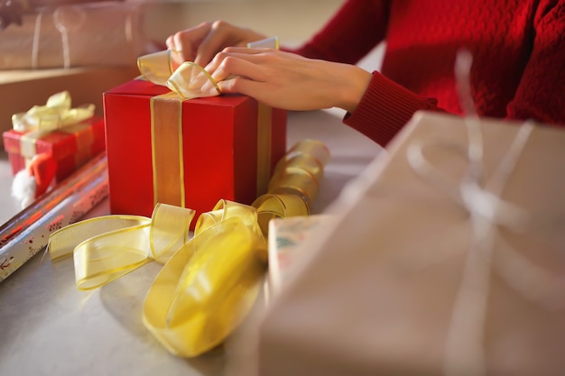 Imballaggio e legatura di un fiocco giallo su una confezione regalo rossa prima delle vacanze di Natale