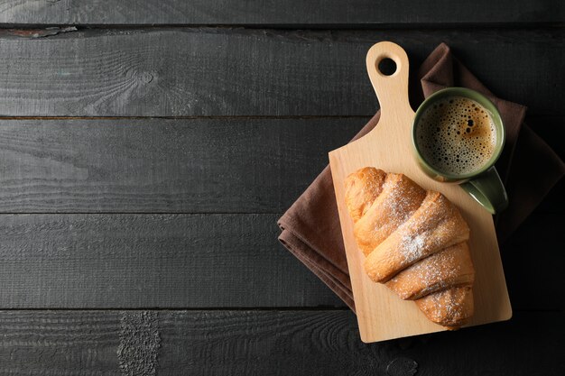 Imbarchi con il croissant e la tazza di caffè su fondo di legno, vista superiore