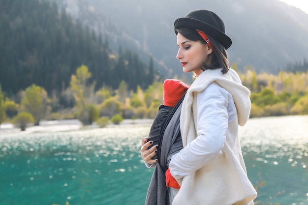 imbracatura all'aperto La madre sta portando il suo bambino e viaggia nel lago di montagna autunnale Concetto di babywearing