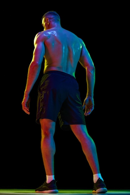 Immagine a figura intera vista posteriore dell'uomo con corpo senza camicia in forma di rilievo muscolare in posa contro il nero