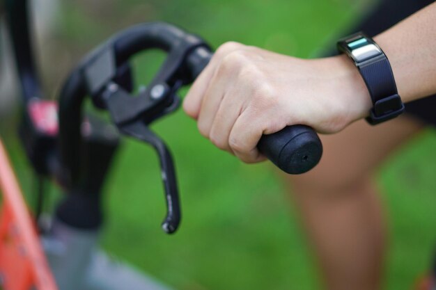 Immagine a fuoco della mano che tiene il manubrio della bicicletta e il polso ha un orologio intelligente nel parco