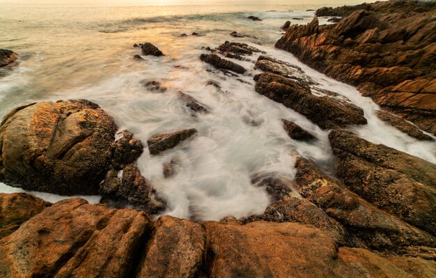 Immagine a lunga esposizione di vista sul mare cielo drammatico con rocce in primo piano tramonto o alba sul fondo del paesaggio del mare.