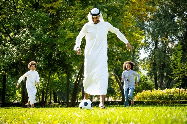 Immagine cinematografica di una famiglia degli Emirati che trascorre del tempo al parco. Fratello e sorella che giocano a calcio nell'erba