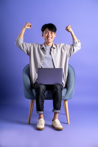 Immagine completa del corpo del giovane uomo asiatico che utilizza il computer portatile su sfondo viola