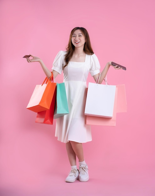 Immagine completa del corpo della donna asiatica che tiene la borsa della spesa e posa su sfondo rosa