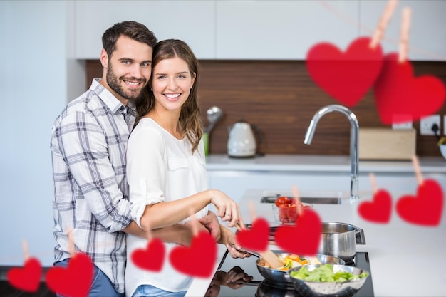 Immagine composita del cuore rosso appeso e delle coppie che cucinano il cibo
