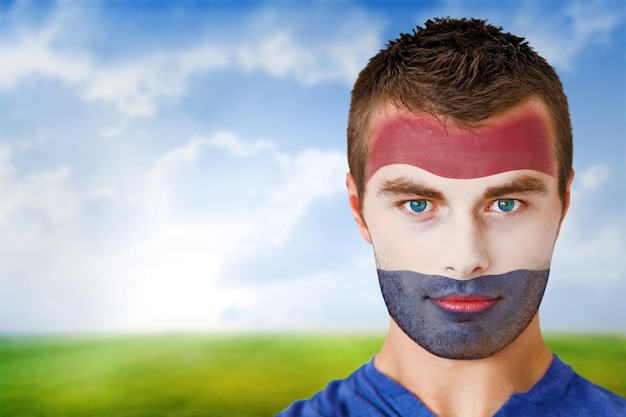 Immagine composita del tifoso olandese in face paint contro il campo da calcio sotto il cielo blu