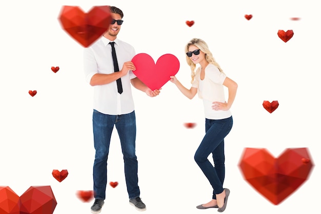 Immagine composita di giovani coppie fresche che tengono cuore rosso