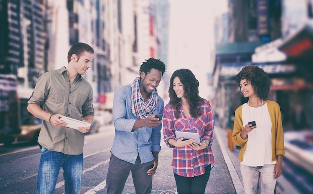Immagine composita di quattro amici alla moda che guardano il tablet e tengono i telefoni