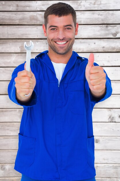 Immagine composita di un meccanico sorridente che tiene in mano una chiave inglese mentre fa un gesto con i pollici in su