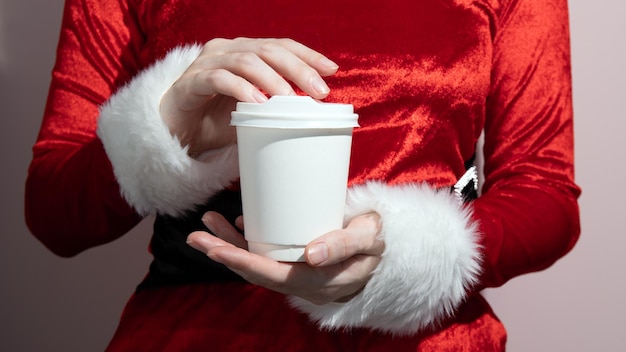 Immagine composita di una ragazza in costume da Babbo Natale che tiene in mano una tazza di carta bianca