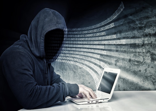 Immagine composita digitale di un hacker che usa un portatile sul tavolo