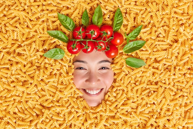 Immagine creativa del volto umano circondato da maccheroni pomodori rossi freschi e foglie di basilico come se i capelli.