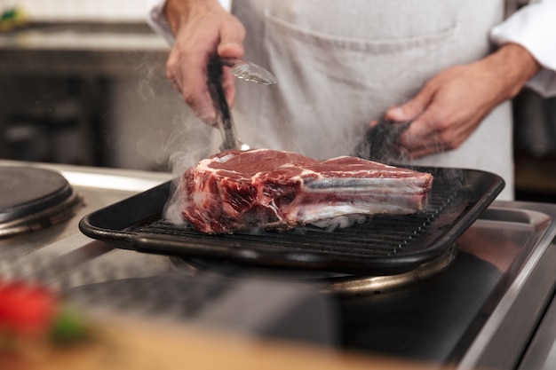 Immagine del capo maschio in uniforme bianca, grigliare carne in cucina nel ristorante