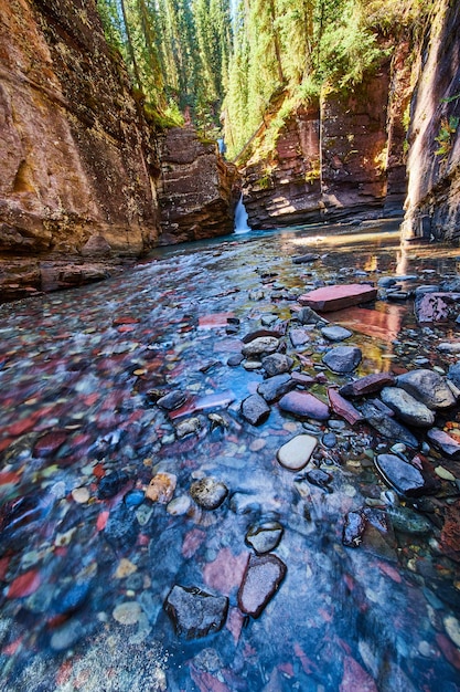 Immagine del fiume di piccole rocce colorate sul fondo della gola con cascata a distanza