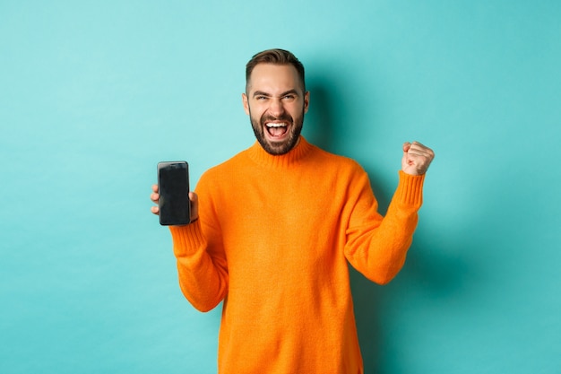 Immagine del giovane felice che vince e mostra lo schermo del telefono cellulare, che si rallegra e celebra la vittoria