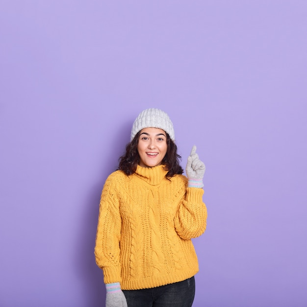 Immagine del maglione d'uso di inverno della bella donna castana, guanti del capand che stanno parete porpora isolata