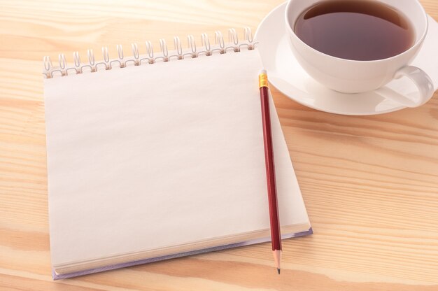 Immagine del mockup. Apra il taccuino della pagina in bianco con uno spazio della copia e una tazza di tè su un fondo di legno bianco della tavola.