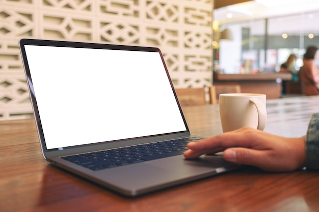 Immagine del modello della mano di una donna utilizzando e toccando il touchpad del laptop con lo schermo del desktop bianco vuoto con la tazza di caffè sulla tavola di legno