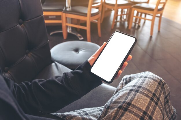 Immagine del modello delle mani che tengono il telefono cellulare nero con schermo bianco vuoto mentre è seduto nella caffetteria